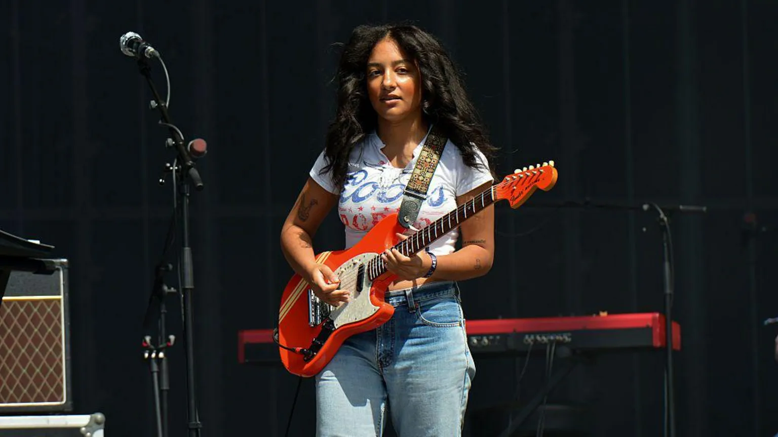 Lily Fontaine, the singer with English Teacher. She is wearing a white T-shirt and jeans, and playing a red guitar.