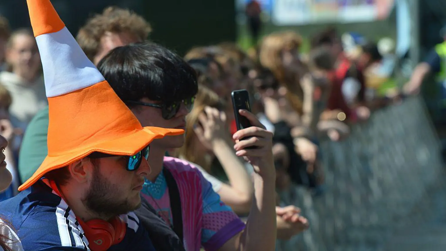 A row of fans at TRNSMT, along a barrier. One of them is wearing a novelty hat shaped like a traffic cone