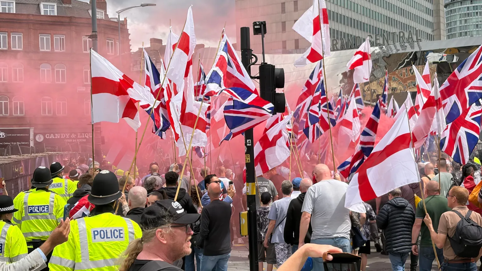 Police can be seen to the side of a group of flag-carrying Britain First supporters. They are carrying Union flags and the cross of St George. 