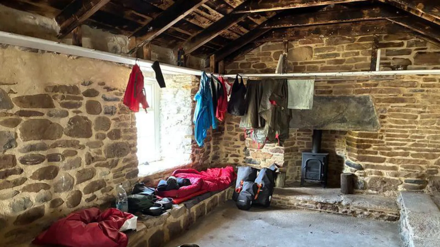 Clothes are hanging upside down to dry inside Burnmouth bothy. A sleeping bag has been set up just next to a stove.