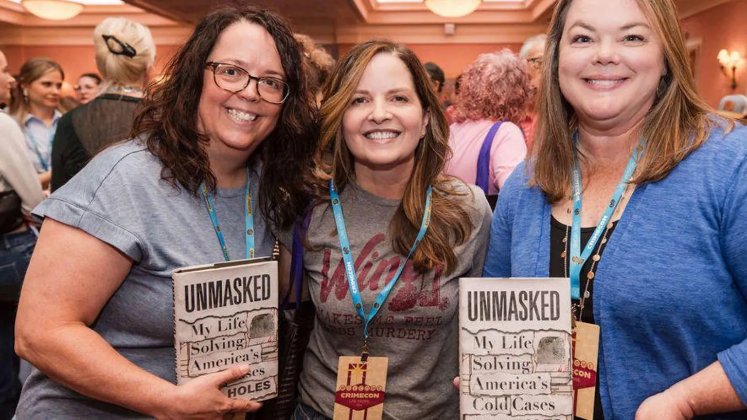 CrimeCon and RenownedPhotos Three female attendees wearing lanyards hold up books titled: 