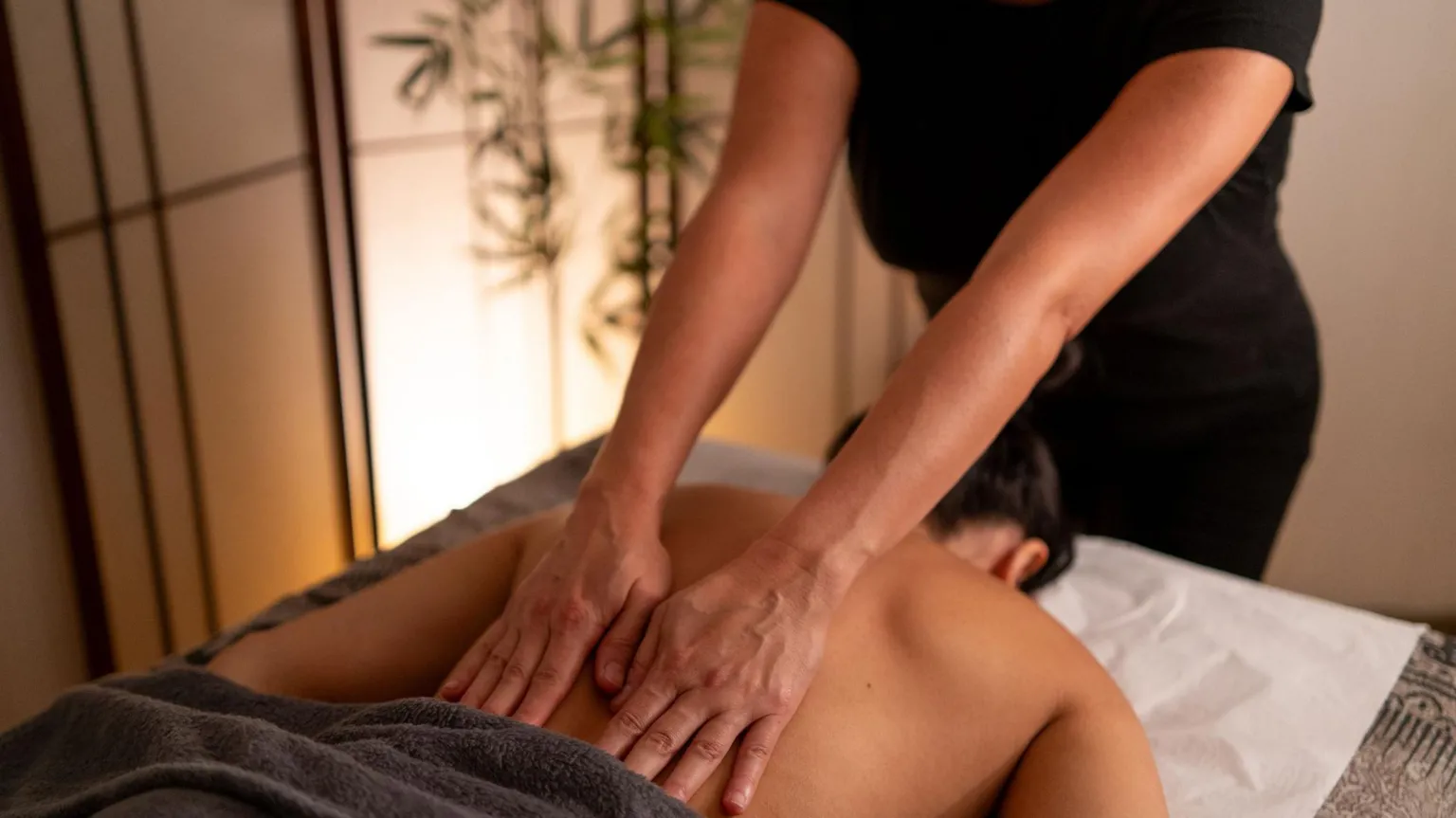 A man lying on a massage table face down. A female masseur has hands on his back