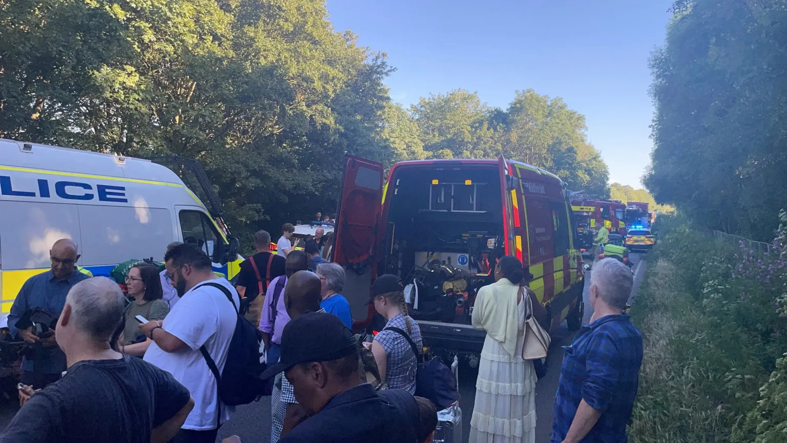 A rural road filled with passengers from the train and emergency service vehicles