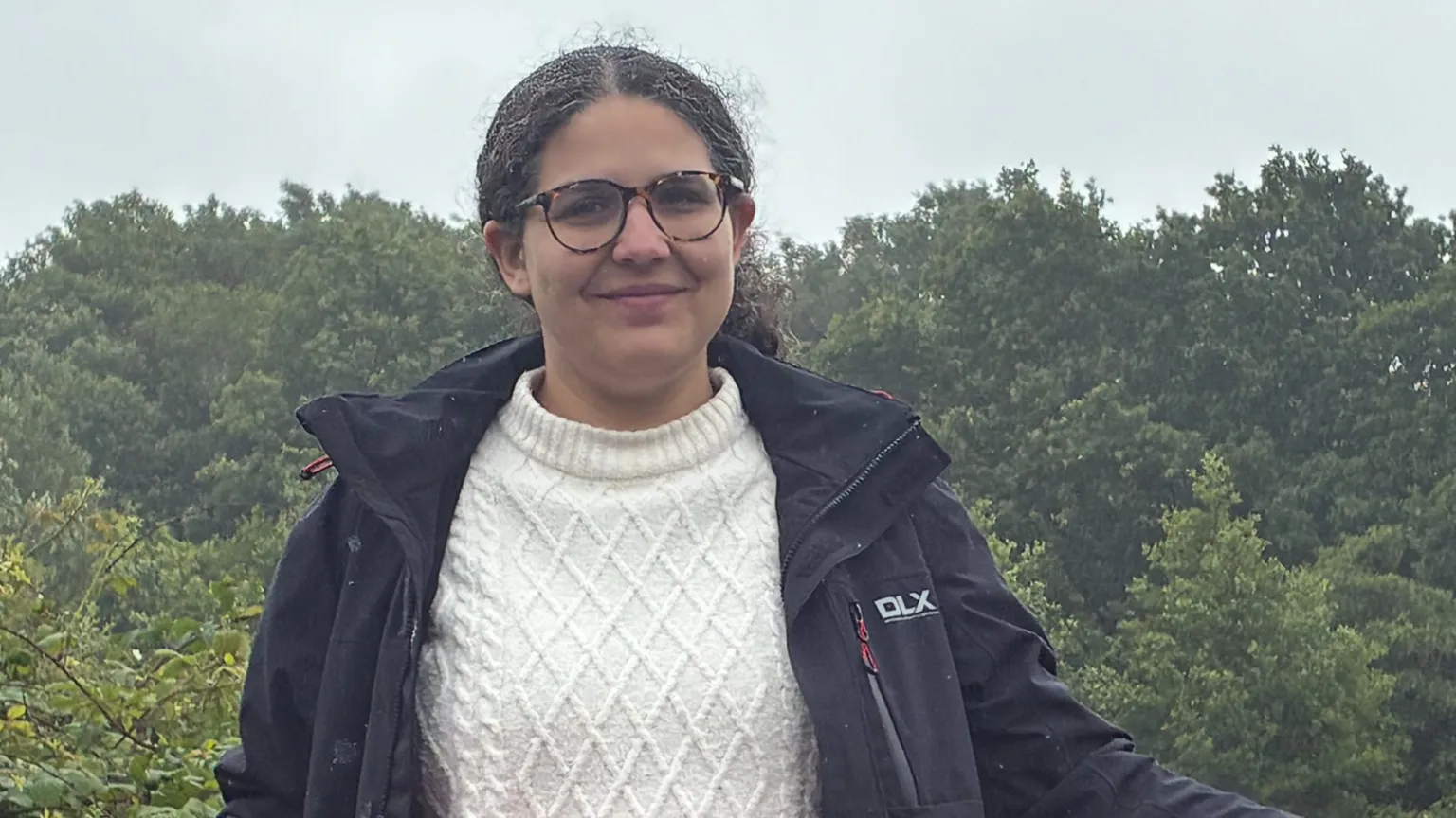 Kieran Molloy A woman with brown hair and glasses, wearing a black jacket and white jumper