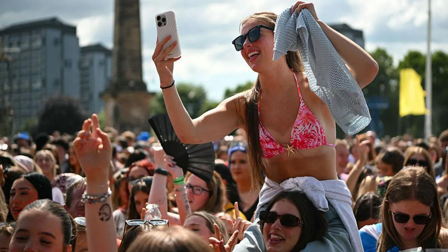  Fans partying in the sun at a music festival, including one woman sitting on the shoulders of her friend