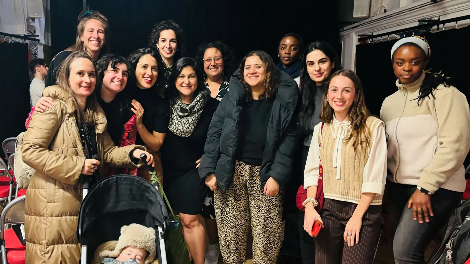 Hera Hussain A group picture of 12 women smiling at the camera. The woman on the far left has a pushchair with a baby in it.