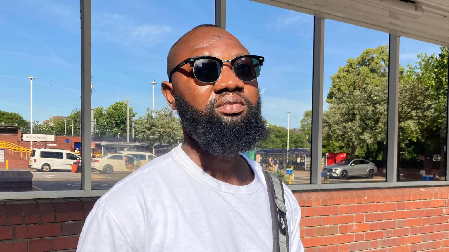 Alex Pope/BBC Nana Adjho, who is wearing sunglasses and a blue t-shirt, at Bedford station