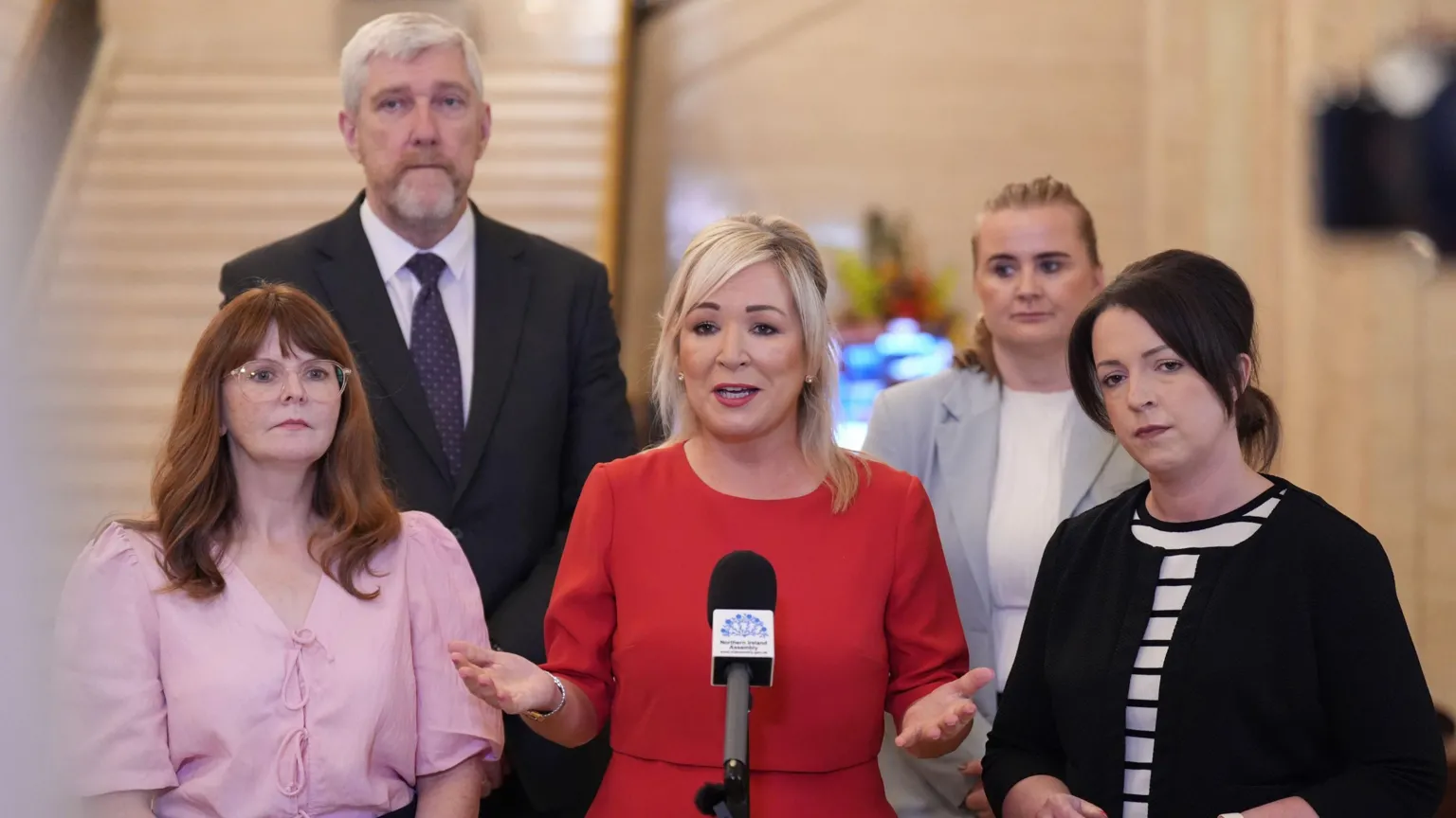 (left to right) Economy Minister Caoimhe Archibald, Finance Minister John O'Dowd, Stormont First Minister Michelle O'Neill, Junior Minister (Executive Office) Aisling Reilly and Infrastructure Minister Liz Kimmins during a press conference in the Great Hall in Stormont, Belfast. O'Neill is speaking into a microphone. She has blonde shoulder-length hair and is wearing a red dress.