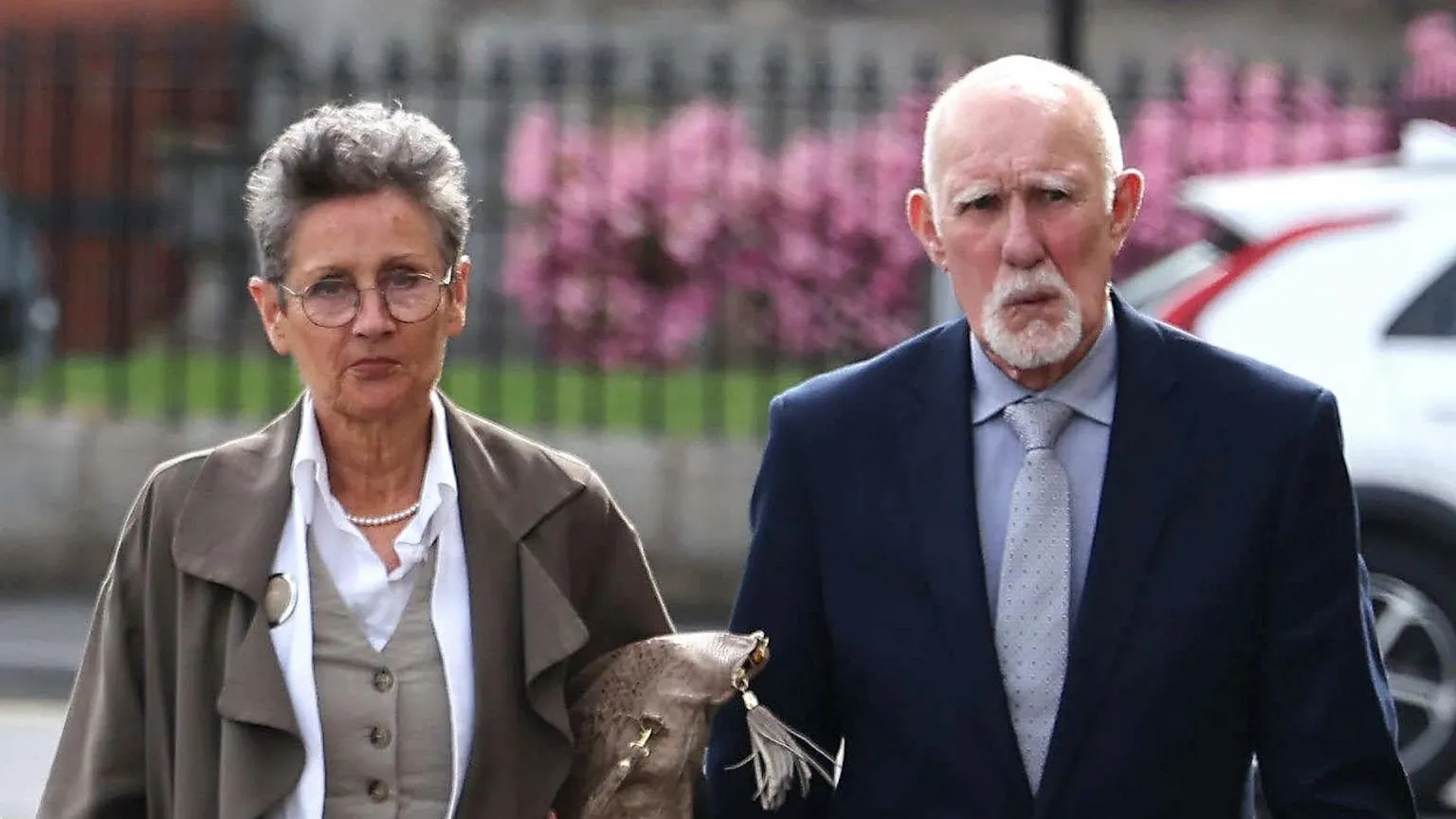 Linda and David Hoy arriving at Newry Crown Court. Linda has short grey hair, wearing glasses, grey waistcoat with white shirt and grey coat. David is bald with white beard, wearing a navy blazer, light blue shirt and light blue tie.