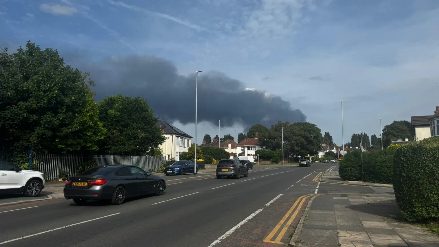 A large plume of smoke can be seen from a pavement at the side of a road in Liverpool.