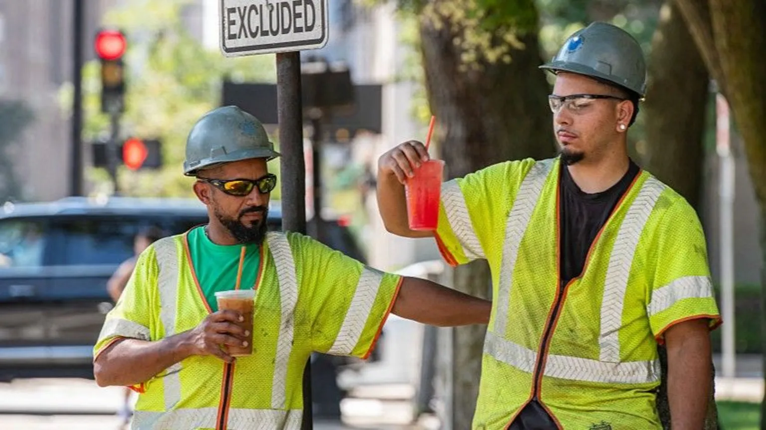 AFP via Two construction workers wearing hi-vis jackets and helmets take a drinks break in Everett, Massachusetts.