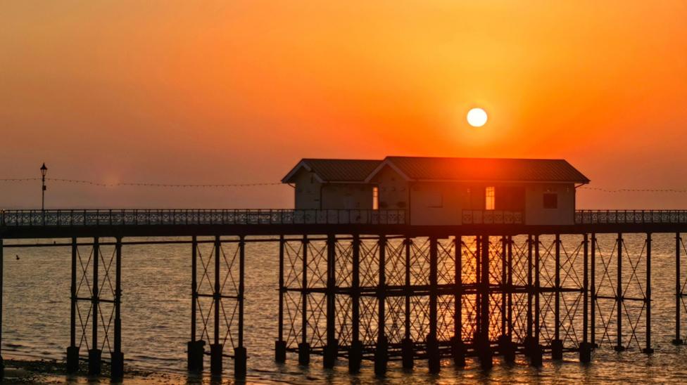 Wooden pier and buildings on the end in orange evening sun which glows bright above