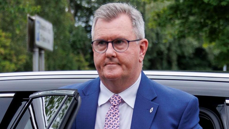 Donaldson wears glasses. He has a navy suit on with a fish pin attached. He's getting out of a car.