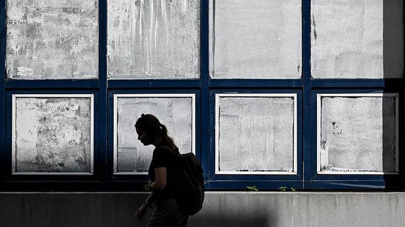 A woman walks past the windows of a school, which have been covered in white chalk
