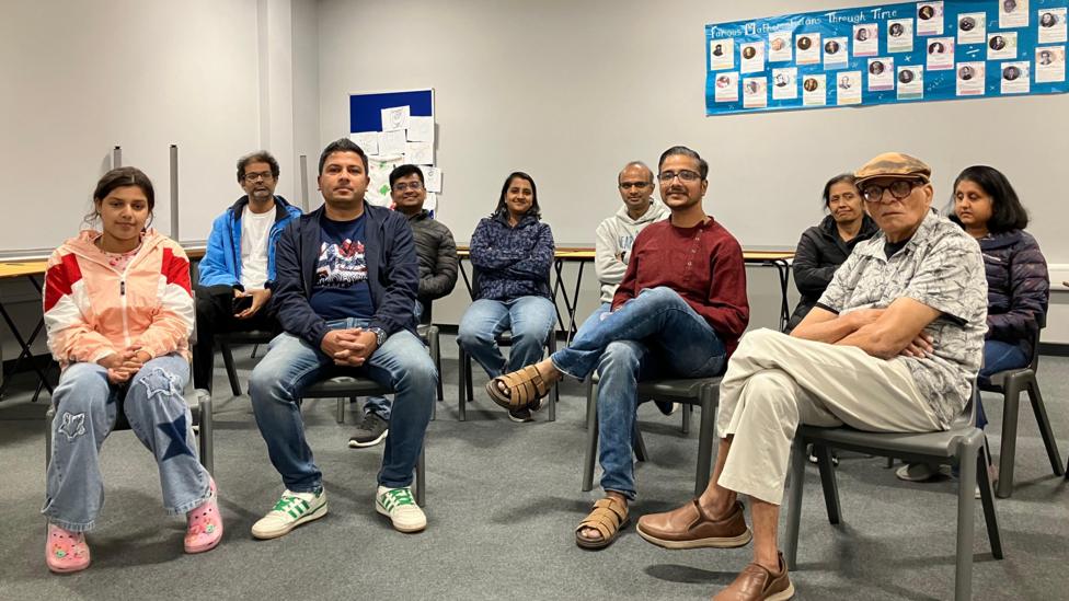 Eight adults and one child sitting in a classroom in two rows. They are looking at the camera.