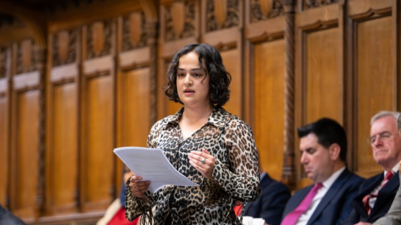 Whittome is a young woman with bobbed, curly black hair and wears a leopard print shirt.