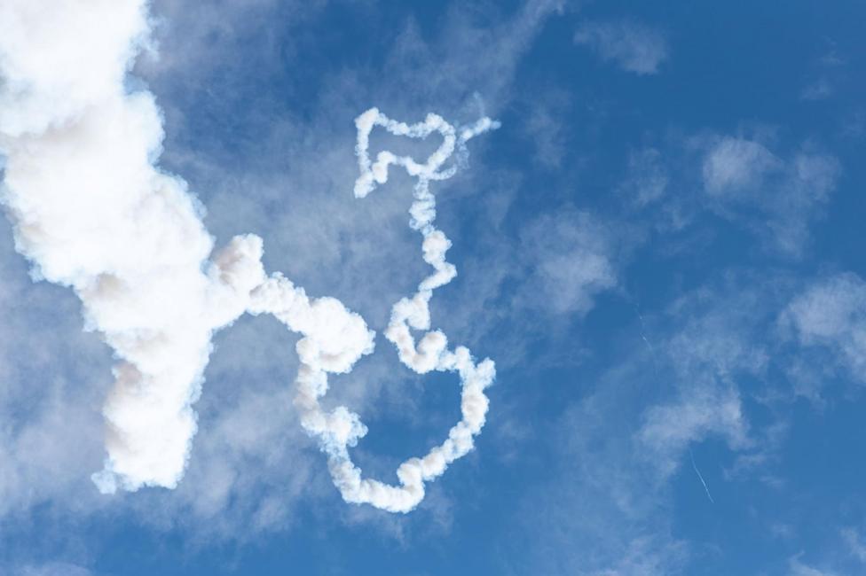 The smoke trail is white and makes a spiral shape against a blue sky with wispy clouds.