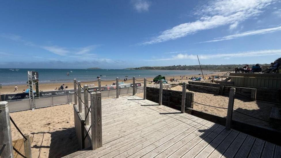 The view from the beach hut's wooden decking showing a long stretch of sand and sea on a sunny day.
