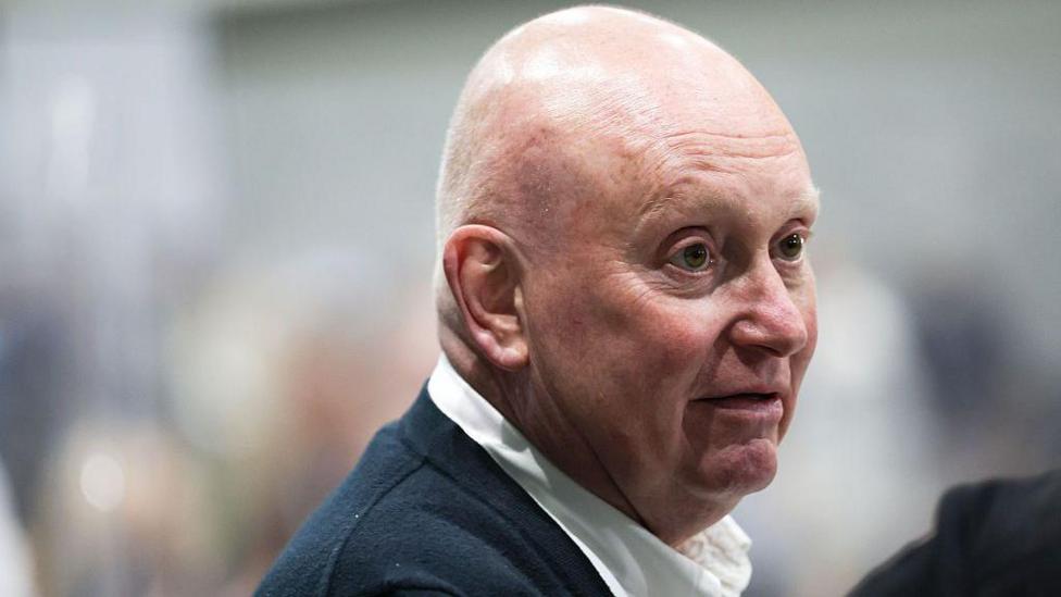 Kevin Lee, a bald middle aged man in open neck shirt, looks on at the Makerfield by-election count