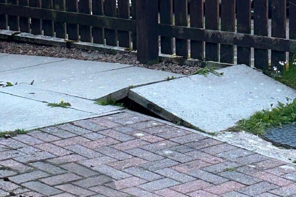 A paving slab which has raised slightly with a fence in the background