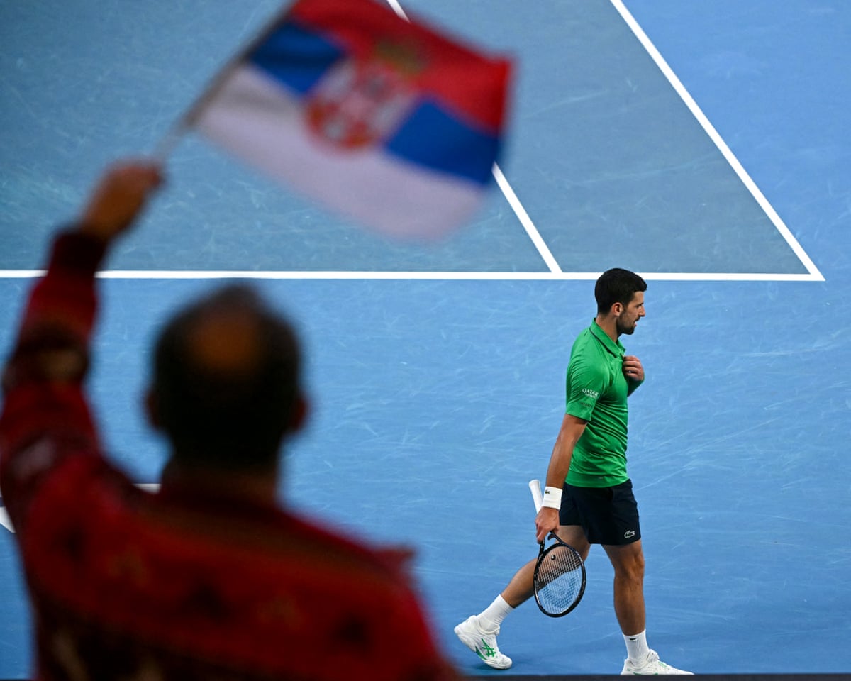 Novak Djokovic walks on the court as a spectator waves a Serbia flag