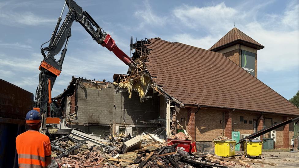 a high-reach excavator tears down a building made of brick