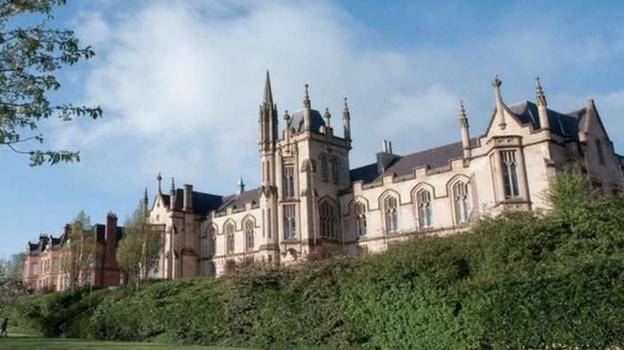 The university campus in Londonderry. A number of bushes and grassy areas can be seen in front of a Gothic-looking building with several large windows.
