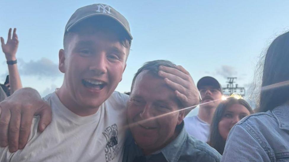 Paul wearing a cap is seen with his arm around his dad who looks emotional.