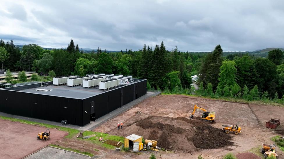 A building site of a new supercomputer. We can see a large black building, with several diggers next to it