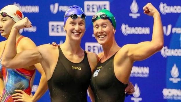Olivia and Georgia Nel in black swimming costumes after a race, with their arms held aloft.