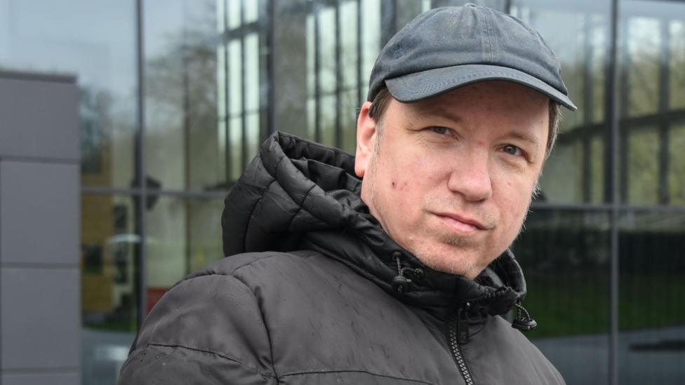 Dirk Hähnel looks at the camera. He is wearing a black jacket and black hat