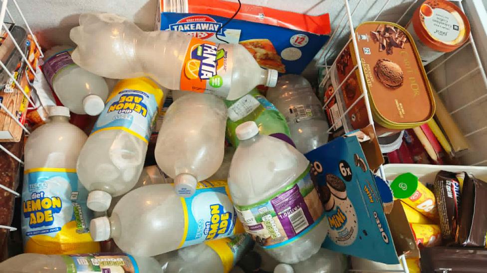 The inside of a freezer stocked with several large bottles of water and other frozen goods 