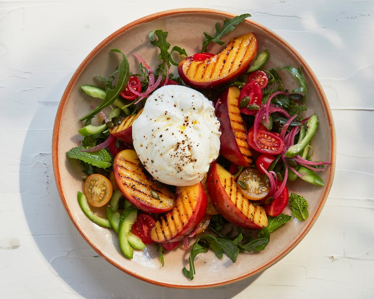 A salad with grilled nectarines, burrata, arugula, tomatoes, pickled onions, and cucumber on a ceramic plate