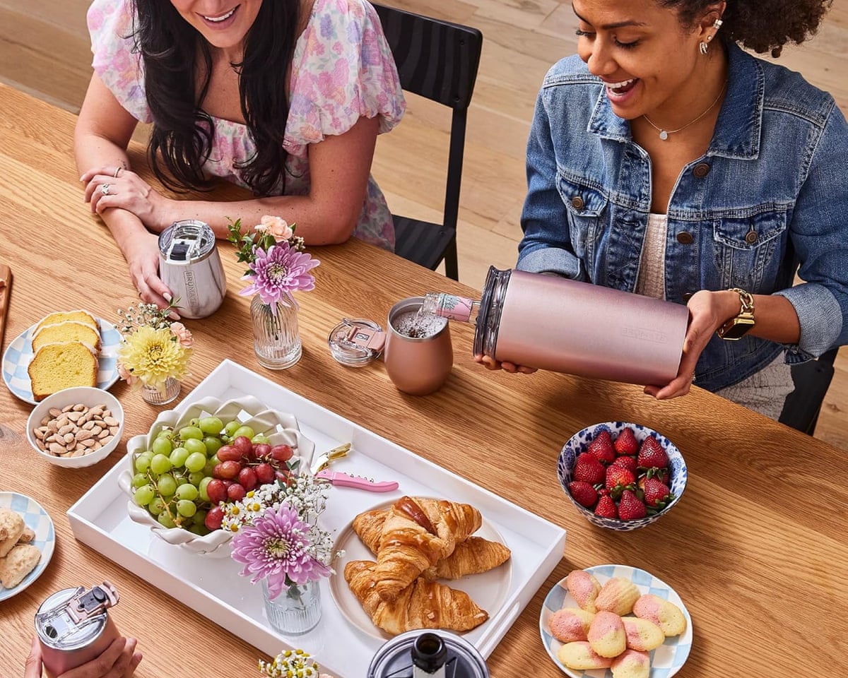 two people sitting at kitchen table with food spread, one person pouring drink out of pitcher