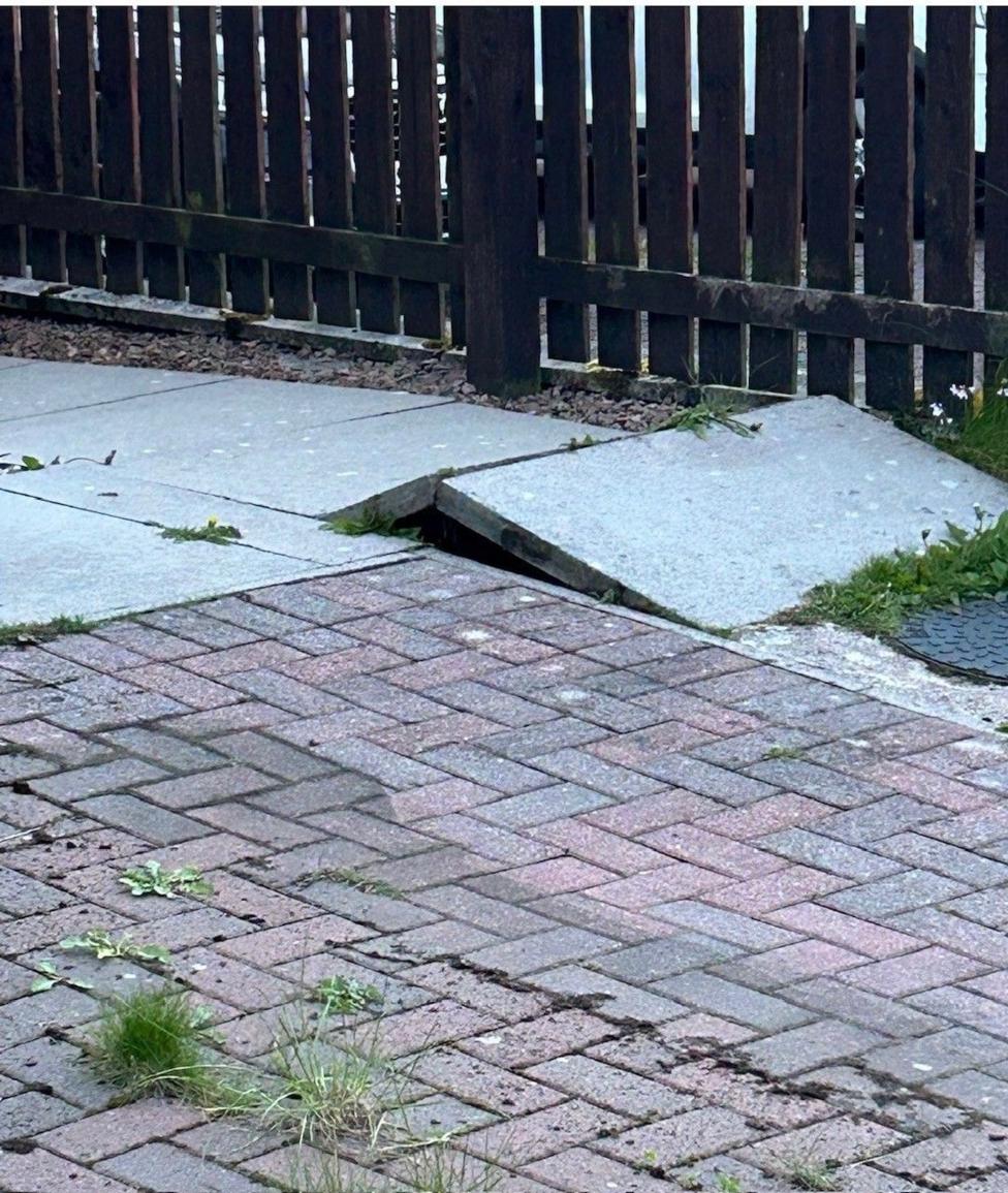 A paving slab which has raised slightly with a fence in the background