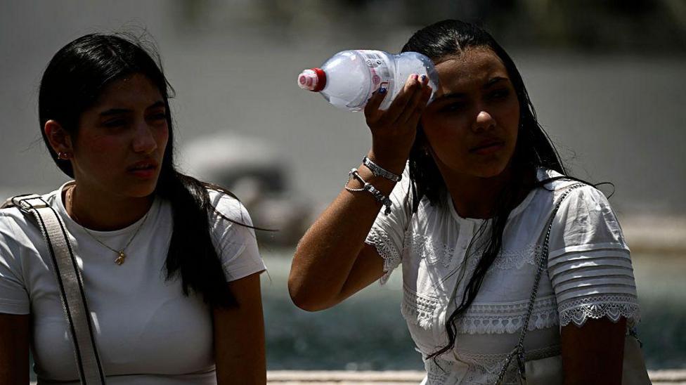 A woman places a bottle filled with ice on her head to cool down at St Peter's Square in the Vatican