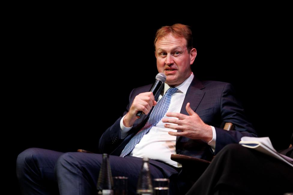 Jim O'Callaghan sitting on a chair with a microphone. He has brown hair and is wearing a dark suit with a blue tie