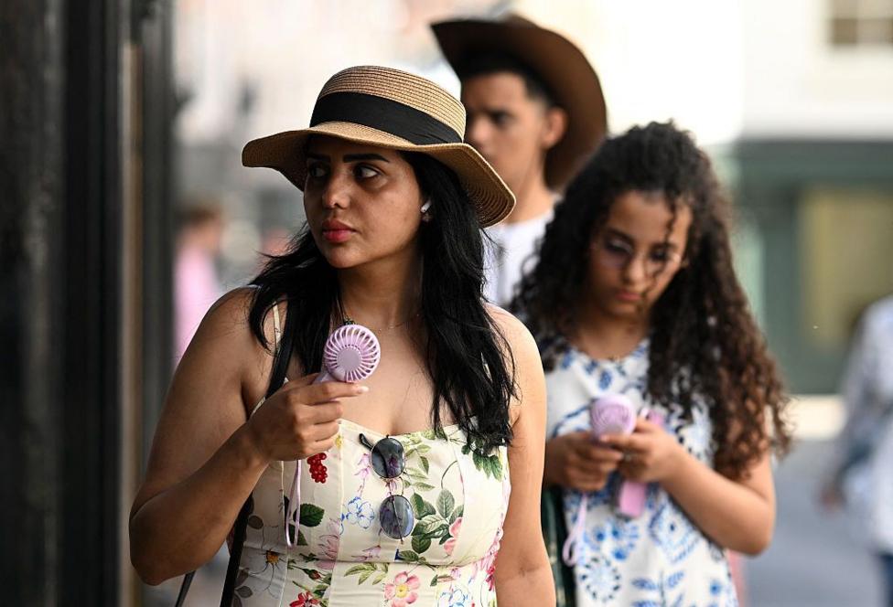 People use hand-held fans to cool themselves as they walk past shops in York, on June 24, 2026. 