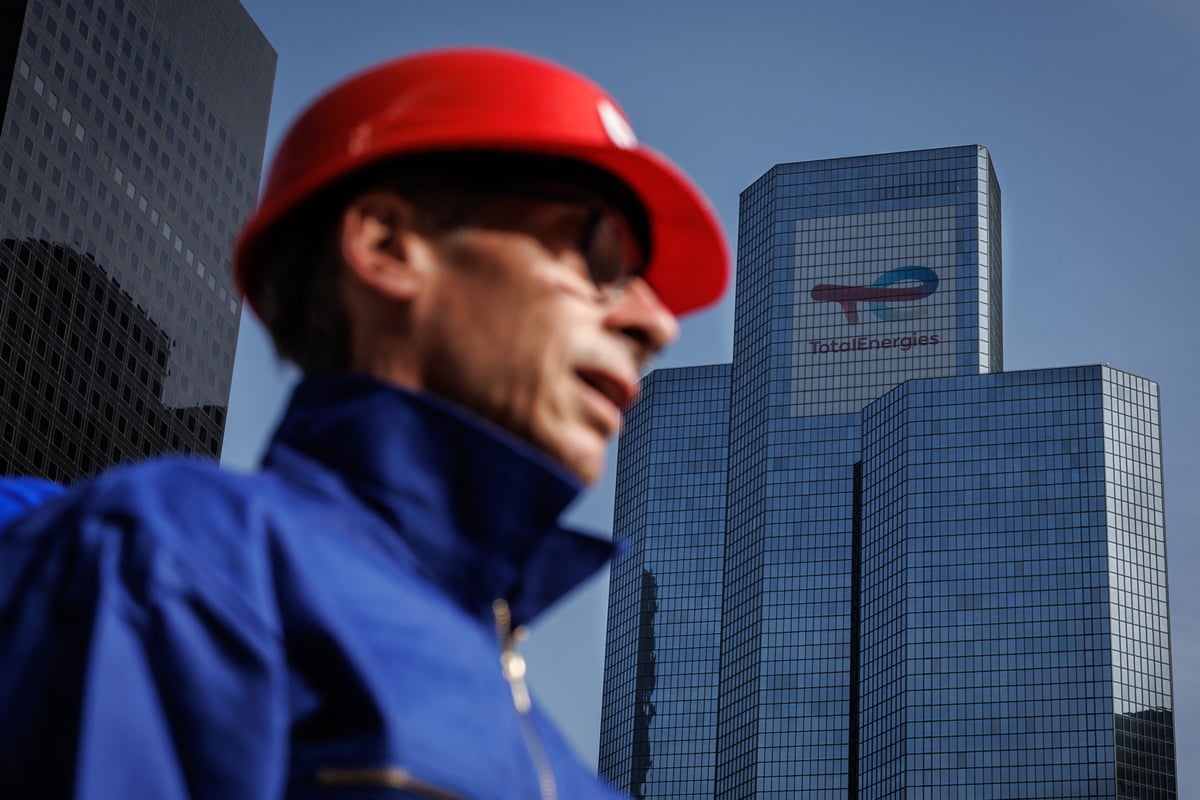 A person dressed as a TotalEnergies worker is photographed with TotalEnergies's headquarters tower in the background