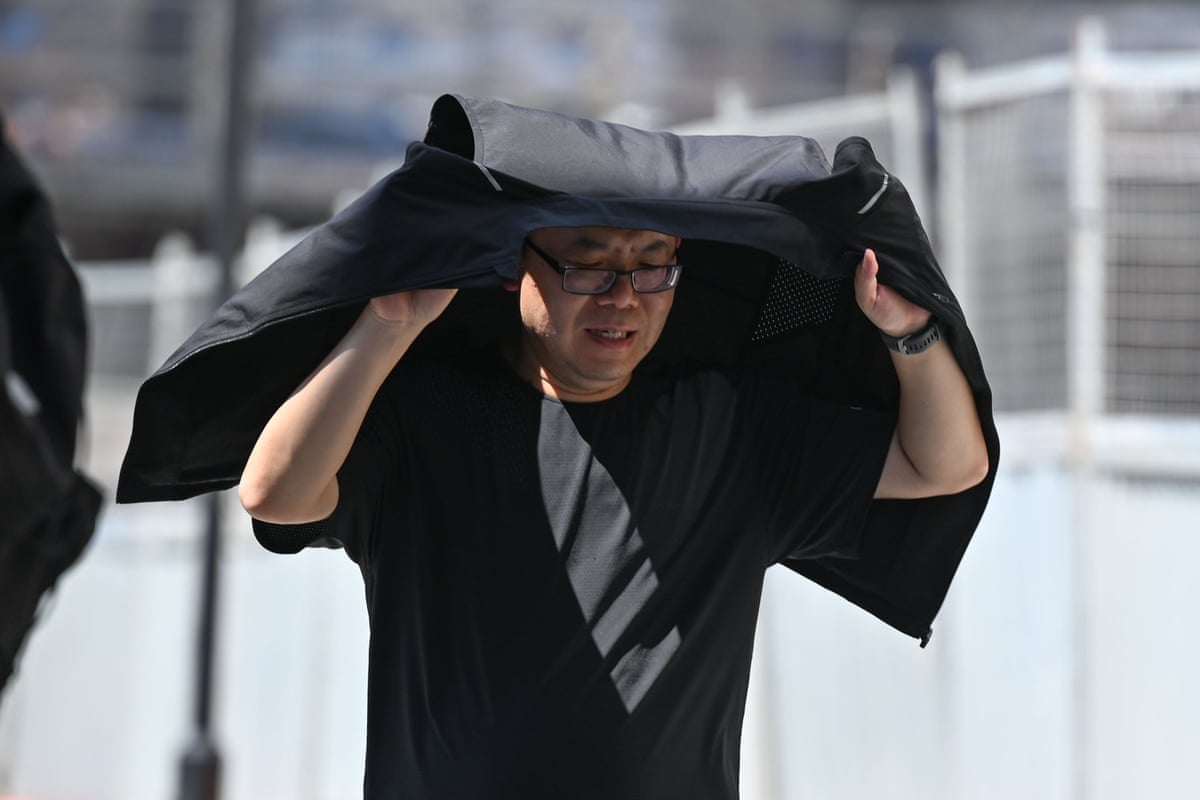 A man hold his jacket over his head as shade as he walks along the street