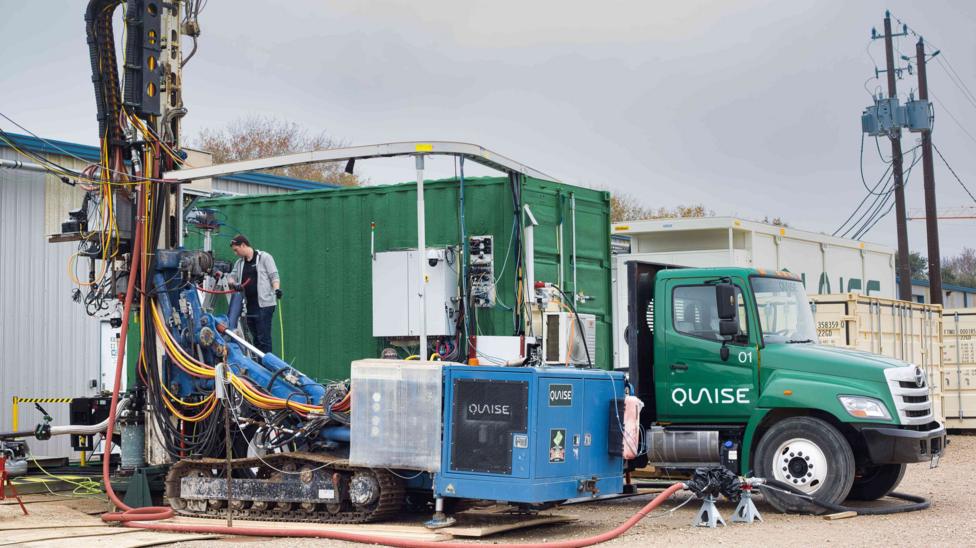 A drill stands in front of a green truck with the Quaise logo