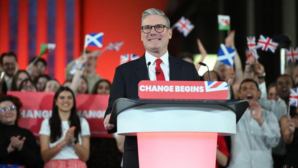 Sir Keir beams at a lectern with the banner that reads 