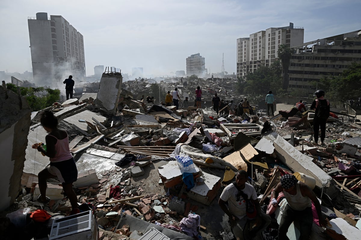 People walk through rubble of collapsed buildings.