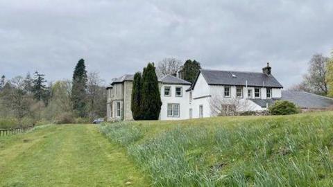A side view of Irvine House a white and granite mansion house surrounded by grass and trees