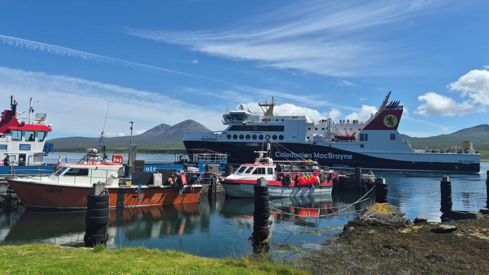 Boats in a port on the Isle of Islay. The ferry is in the water in the background and smaller fishing boats are in the foreground. 