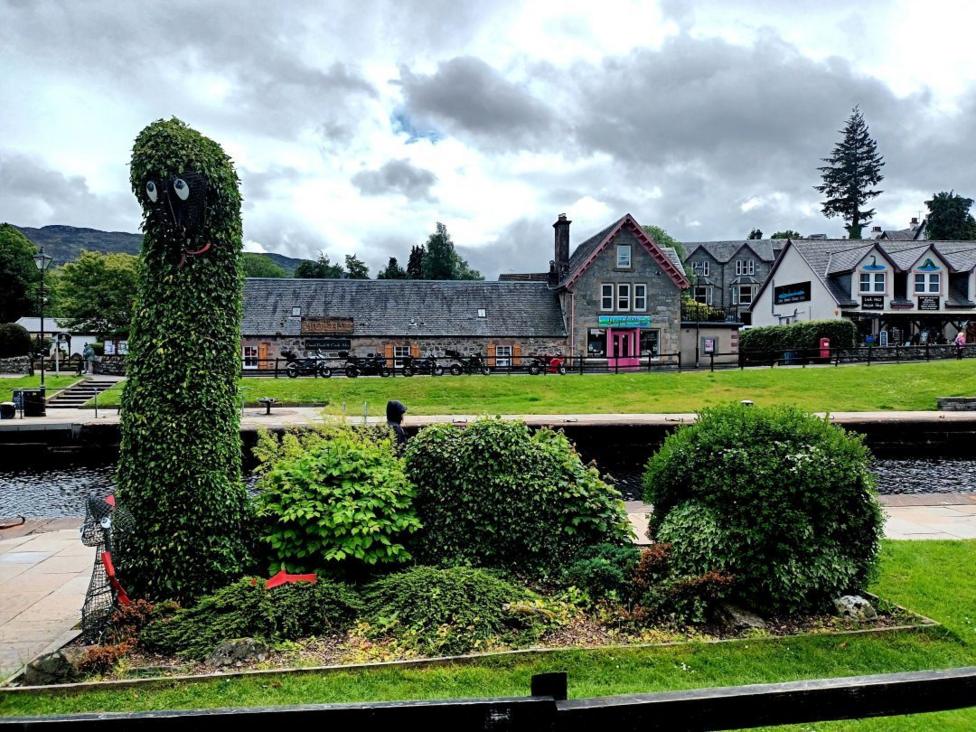 A group of bushes trimmed into the shape of the Loch Ness Monster. There are buildings and a park in the background.