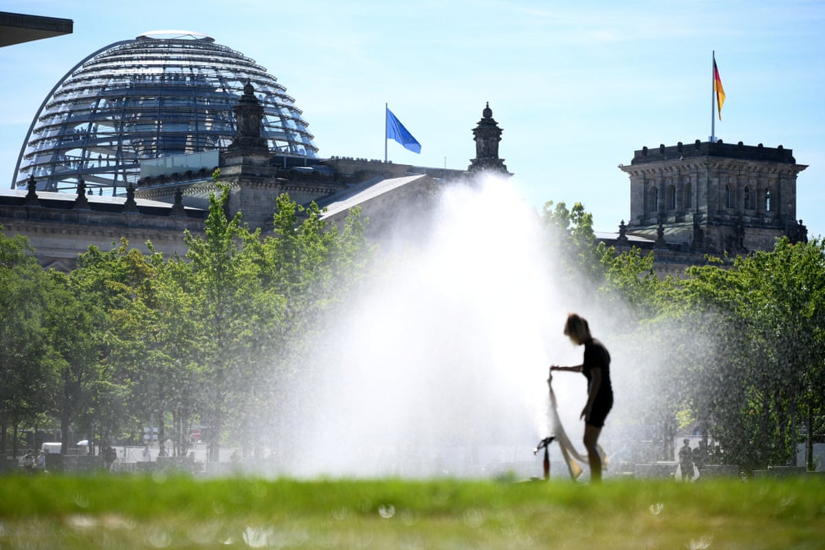 The dome and building of the Reichstag, seat of the lower house of German parliament Bundestag, are seen in the background as a woman soaks a piece of clothing in the water stream of a sprinkler system in Berlin.