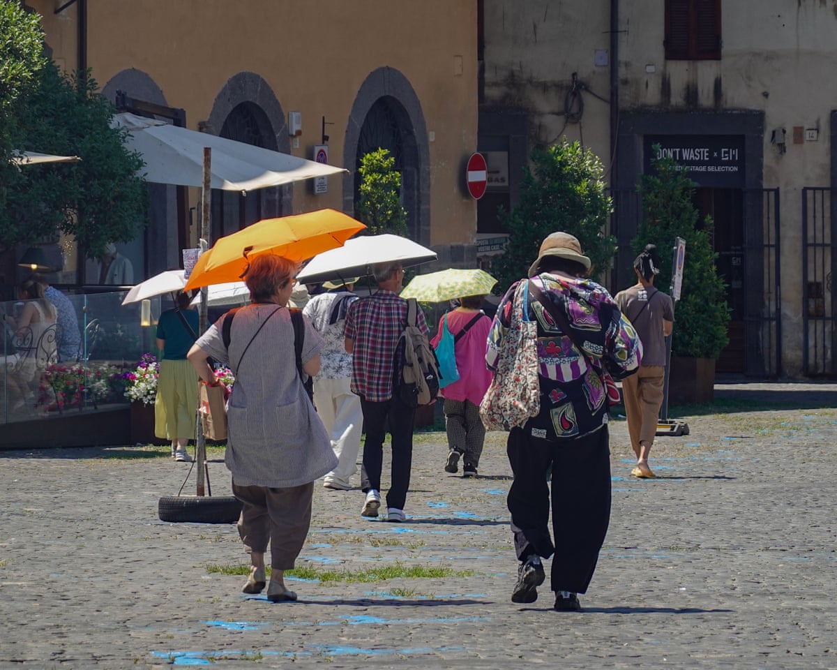 Pedestrians use umbrellas for shade while walking through Orvieto, Umbria, Italy.