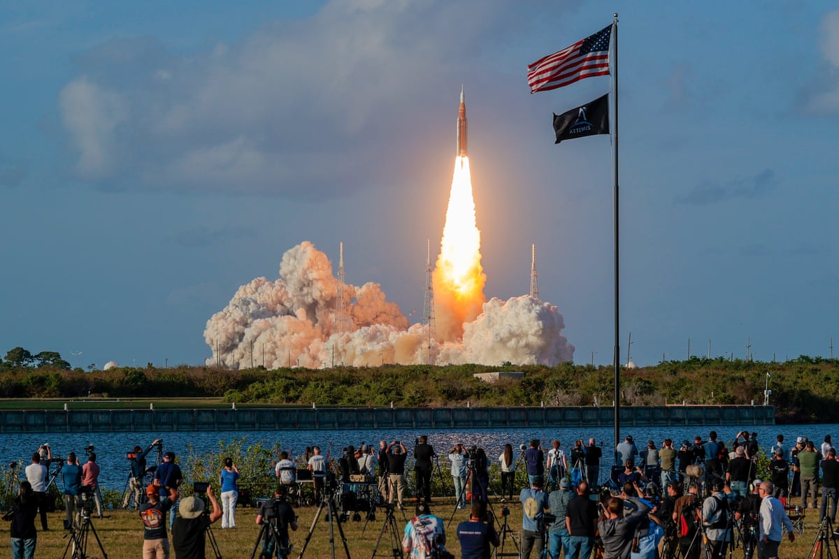 The fire and smoke as the rocket lifts into the air, watched by people in the foreground