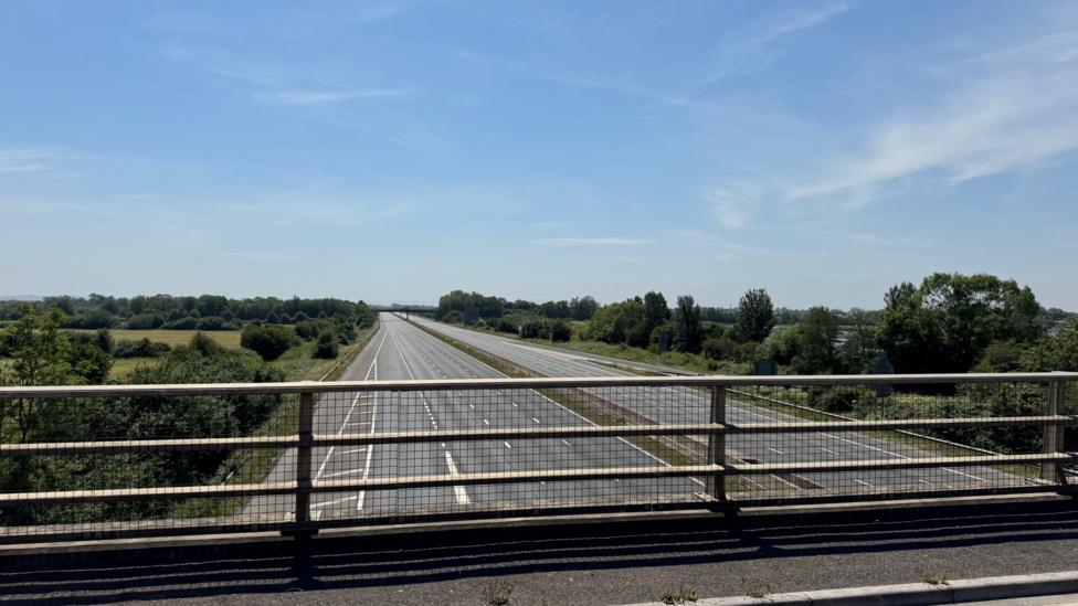 Picture from the motorway bridge of an empty road and motorway. There is blue skies in the background.